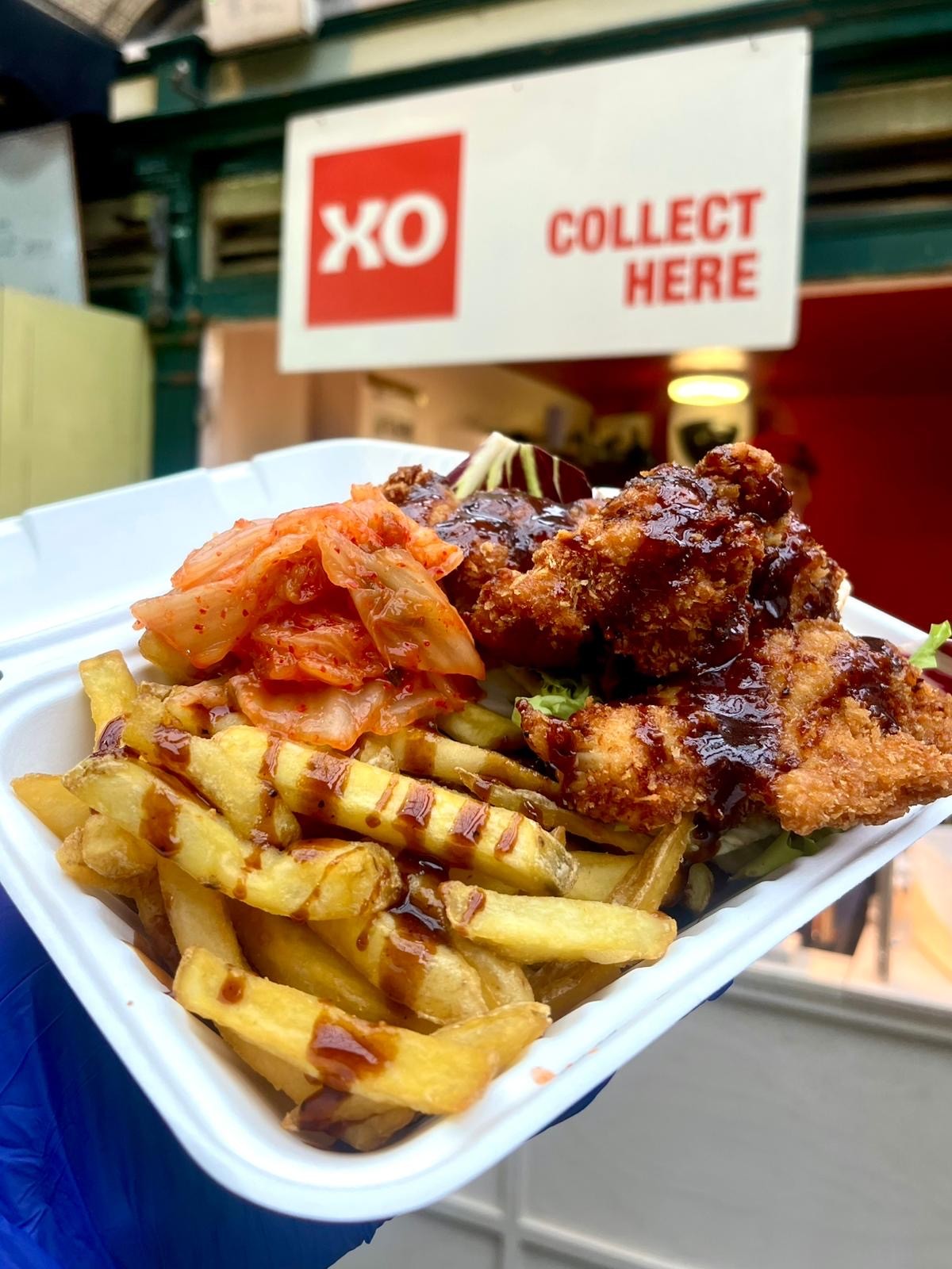 Container from XO with fries and Korean fried chicken in, topped with a sauce