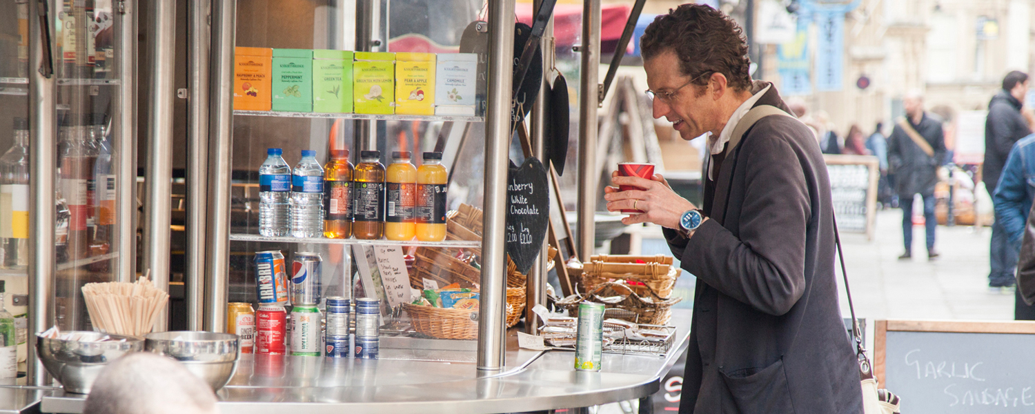 A man with a drink in his hand at a market stall