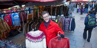A smiling man holding up some jumpers in a market place