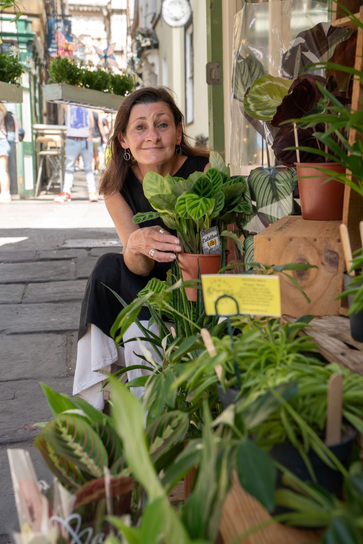 A lady smiling and crouching next to some plants