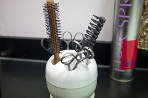 A comb, brush and some scissors in a white pot