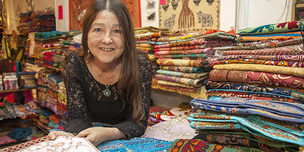 A lady with long hair smiling, with piles of fabric behind her