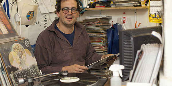 A man holding a record, sat behind a record player
