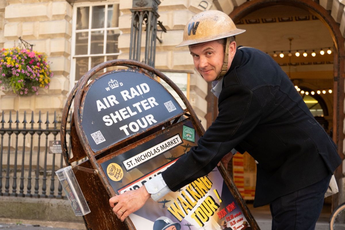 A man dressed as a world war 2 warden with an air raid shelter tour sign