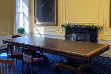 A small bright room with a period-style table and chairs facing it.