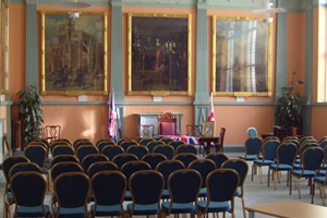 A large room with large paintings on the wall and many rows of chairs